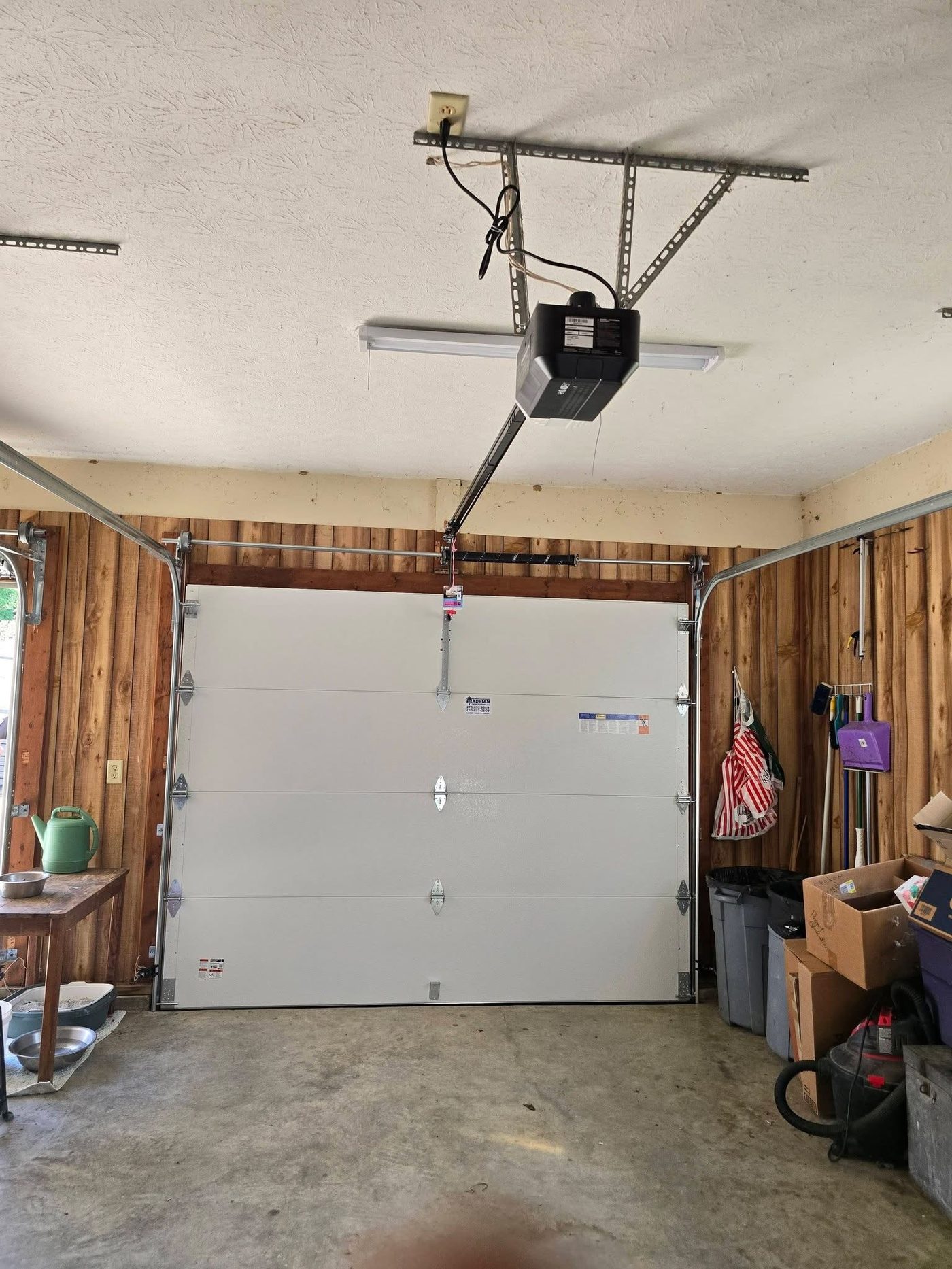 Completed garage door and opener installed in a wood-paneled garage